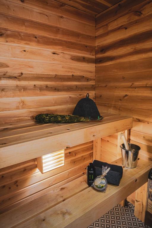 A private sauna is presented with warm wooden walls and benches, providing a cozy environment. Relaxation items, including a small bucket and toiletries, are displayed on the lower shelf. Soft lighting enhances the tranquil atmosphere, inviting guests to unwind after a busy day.
