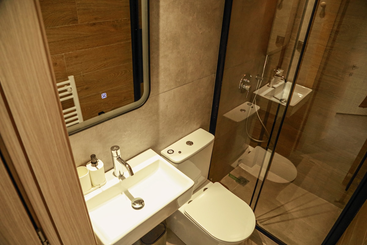 A modern bathroom features a glass-enclosed shower and a sleek vanity with an integrated sink. Soft lighting is provided by an overhead fixture, and neutral tones enhance the contemporary design. A towel rack is positioned near the shower for convenience.