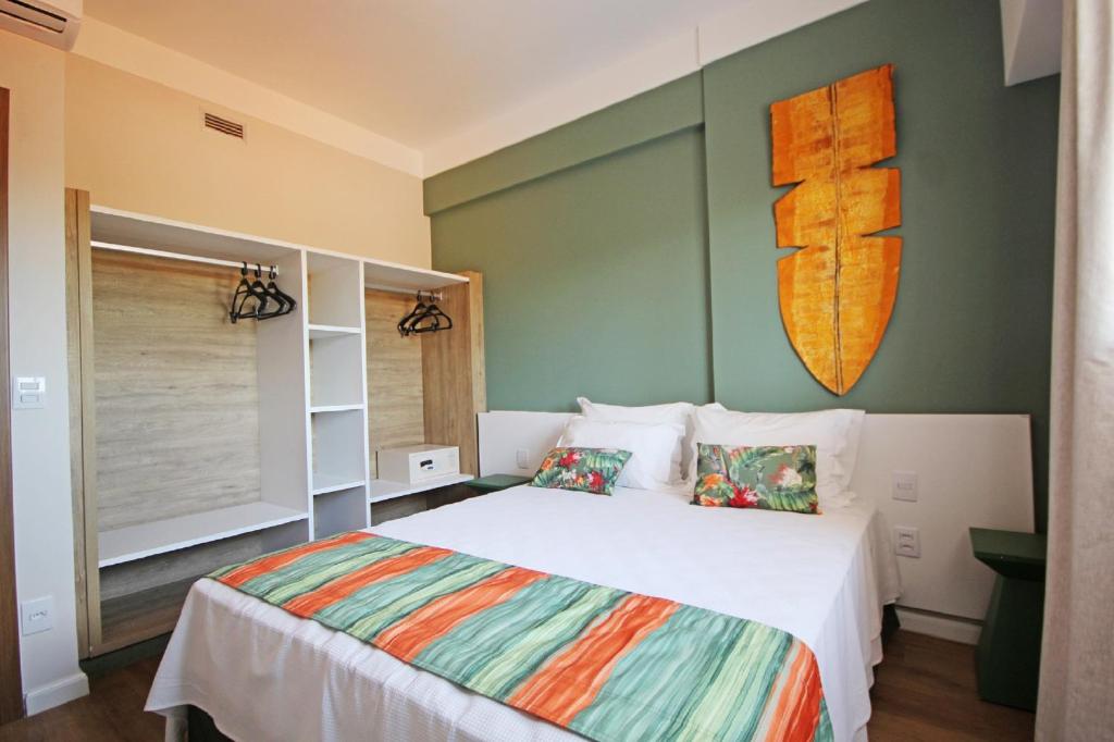 A sleeping area features a spacious bed adorned with decorative pillows and a colorful bed runner. A minimalist closet with hangers is present, alongside an artistic wall piece that adds character to the room. Natural light filters through a nearby window.