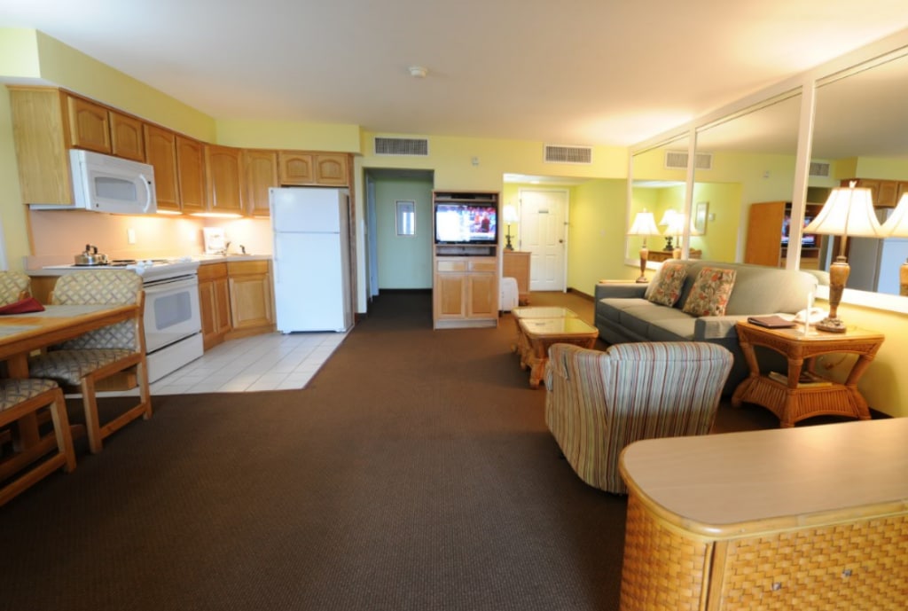 A spacious living area features a comfortable seating arrangement, including a sofa and armchair. A dining nook with barstool seating is positioned near the kitchen, which is equipped with modern appliances. Soft lighting from table lamps creates a warm ambiance throughout.