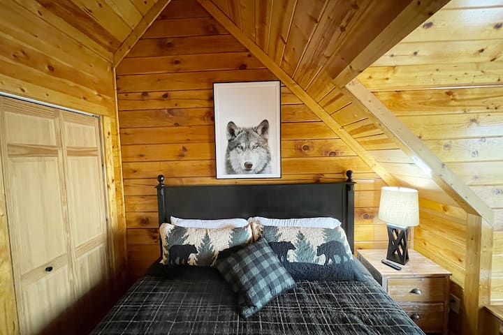 "Mbwa mwitu Den" huwa na kitanda aina ya king, samani za chumba cha kulala cha rangi nyeusi na kahawia, runinga kubwa janja, beseni la jacuzzi na bafu lililounganishwa.