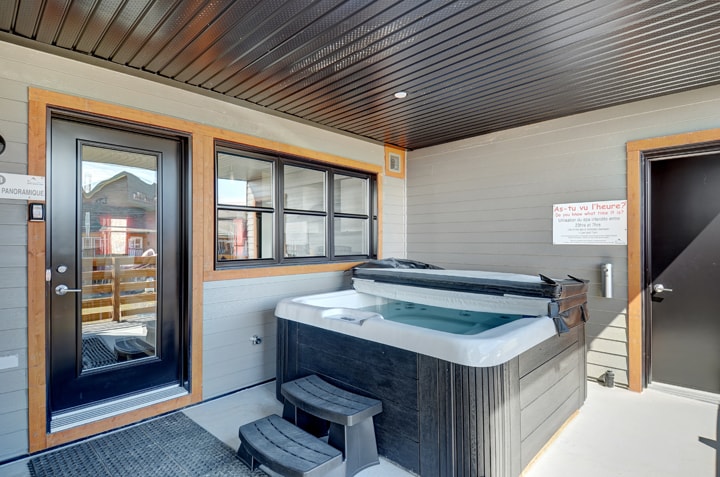 A private spa is situated on a covered patio, surrounded by wooden accents. The entrance features large glass doors and a black door, providing access to the condo. A small set of steps leads up to the spa area, enhancing accessibility.