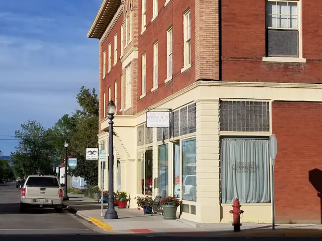 The historic 1908 Grabow Hotel building is displayed from the corner view, featuring red brick walls and large windows. The ground level includes a storefront with a sign and decorative flower pots, while a streetlamp and fire hydrant are visible along the sidewalk.