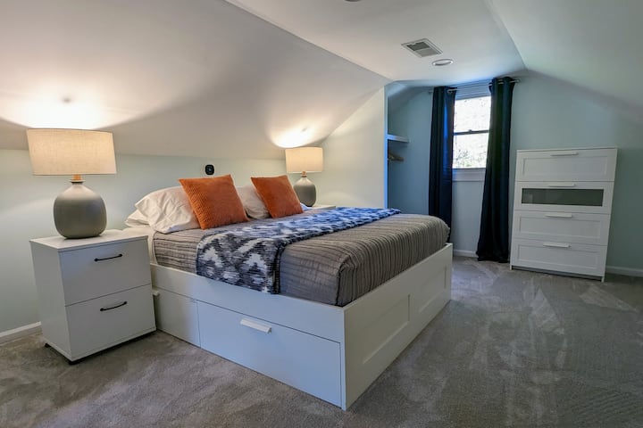 Bedroom #3 on the second floor with a queen bed, a bedside power station, a desk, and blackout curtains. The bed has a memory foam mattress. Please note that access to the upstairs is through Bedroom 1.