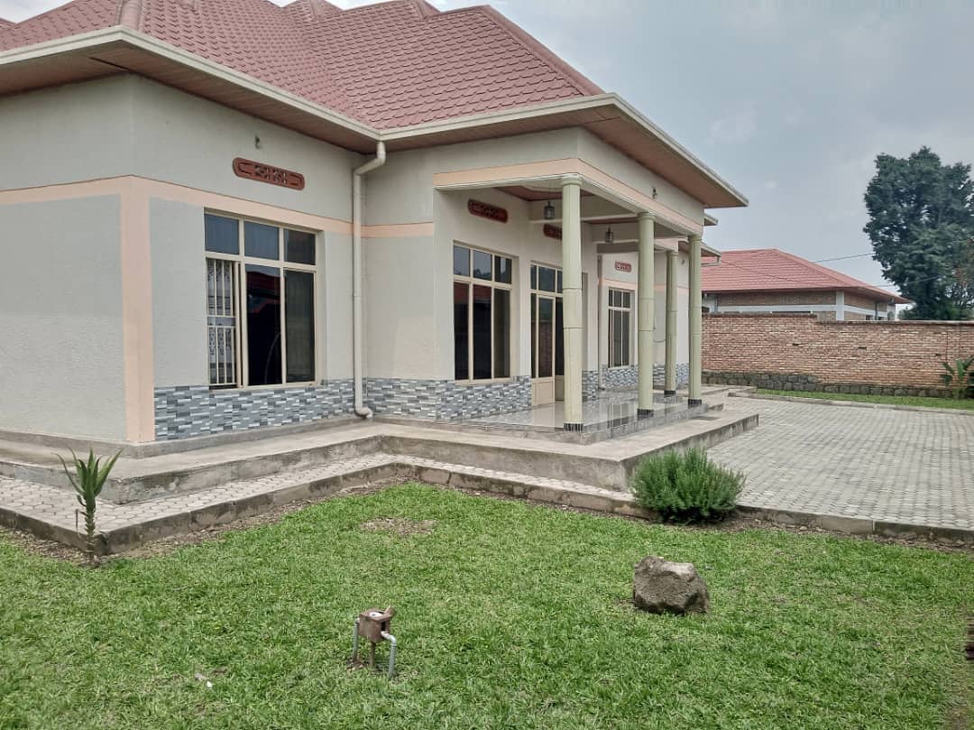 The exterior of a spacious home is displayed, featuring a smooth stone foundation and multiple large windows. A well-maintained lawn surrounds the entrance, which includes a covered porch with decorative columns. Nearby, a small garden area adds a touch of greenery.