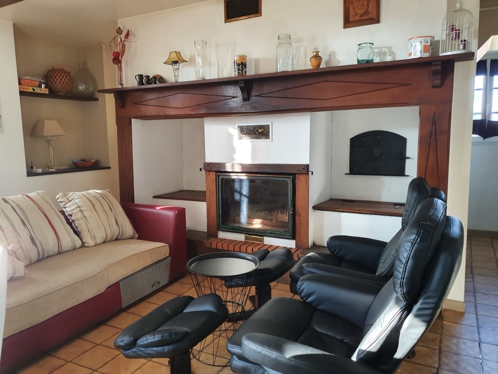 A comfortable seating area is highlighted by a modern two-tone sofa and black reclining chairs. A wooden fireplace with shelves is positioned in the background, adorned with decorative items and glassware. Warm lighting fixtures enhance the cozy setting.