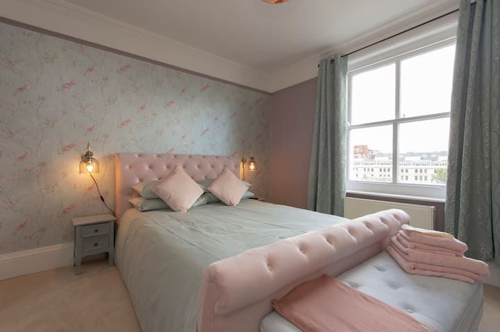 Dormitorio 2 (en suite): cama de terciopelo rubia de tamaño amable con otomana azul bebé.