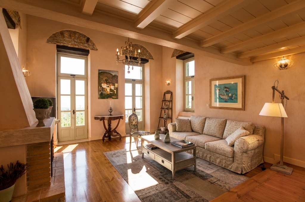 A spacious living area features large windows that allow natural light to fill the room. A comfortable sofa is positioned around a low coffee table, complemented by a decorative rug. Artwork adorns the walls, enhancing the room's inviting atmosphere.