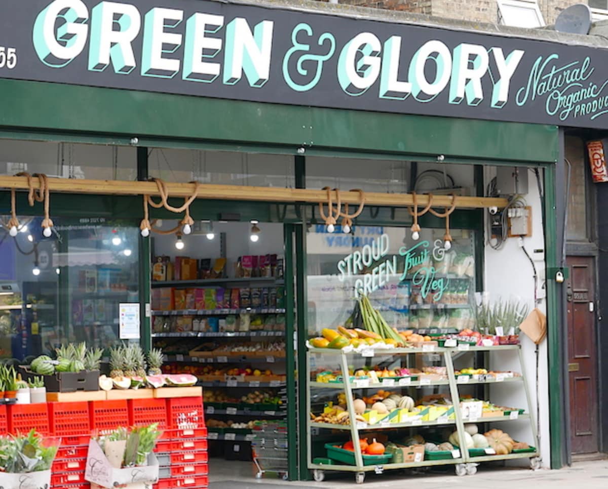 A storefront displays an array of fresh produce, with vibrant fruits and vegetables arranged neatly on tiered shelves. Warm lighting and clear signage highlight the emphasis on natural and organic products. The entrance is framed by green accents and wooden elements, inviting visitors inside.