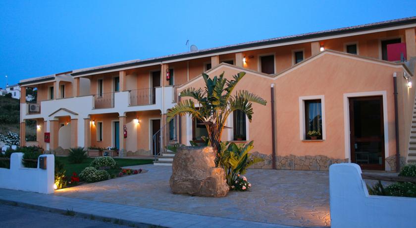 The hotel exterior is highlighted by warm-colored façades and elegant stone accents. Lush greenery and well-maintained flowerbeds surround the entrance, creating a welcoming environment. Outdoor lighting enhances the building's features as twilight settles, with spacious balconies accessible from the upper level.
