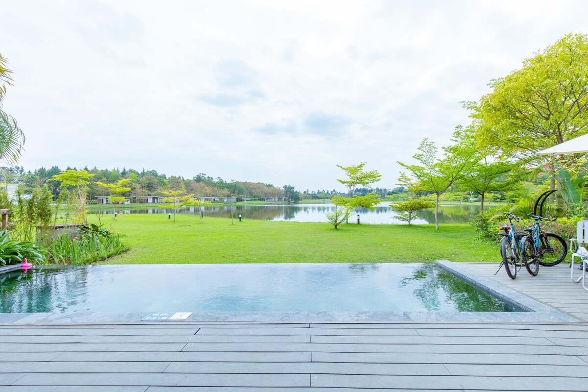 An outdoor area features a private pool overlooking a serene lake, framed by lush greenery. Two bicycles are positioned nearby, inviting exploration. The wooden decking extends toward the water, enhancing the tranquil ambiance.