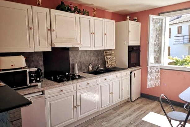 The kitchen features white cabinetry paired with a dark countertop, complemented by modern appliances including a microwave and coffee maker. A window allows natural light to fill the space, while decorative elements enhance the room's charm. A table with chairs provides a cozy dining area.