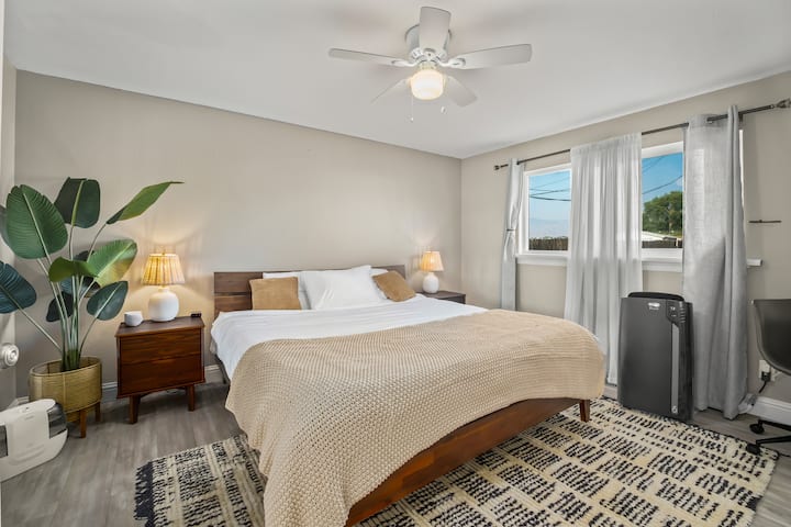 Bedroom #3 - Master suite, king bed (Zinus memory foam), two nightstands with lamps, charging outlet on left nightstand, HomePod Mini, humidifier, luggage rack, and closed door work desk on right side with portable wireless charger. 