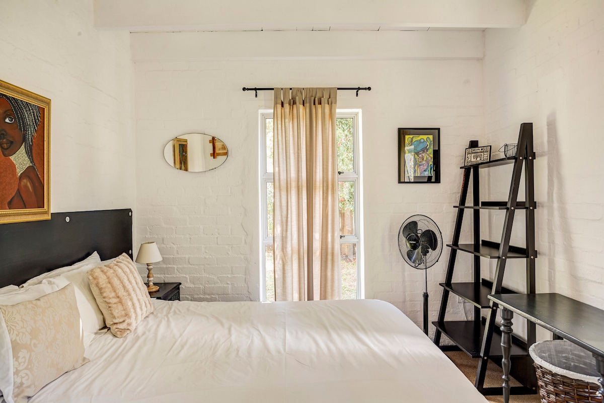 Mountain Room has windows facing the garden and is the quietest room in the house. 

The walls show off original African art by local artists.

Pack out your luggage on the shelves or use the table as a work station.

Cooling fans in each bedroom.