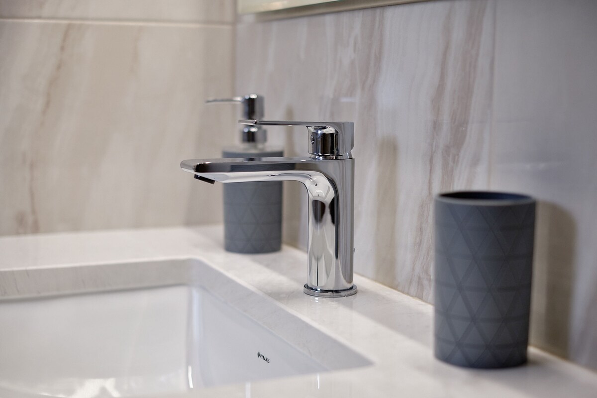 A modern bathroom sink area features a sleek chrome faucet and a white sink. Two gray decorative cups are placed on the marble counter, complementing the elegant design with subtle textures.