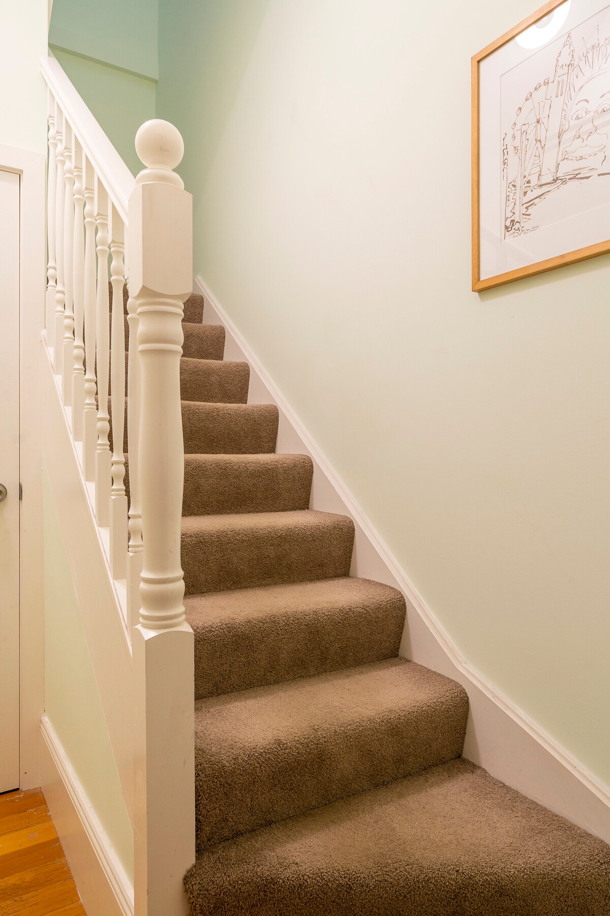 A carpeted staircase is featured, leading to a studio. The walls are painted in a soft mint color, with a simple artwork hanging near the top. The railing is white, complementing the overall design.