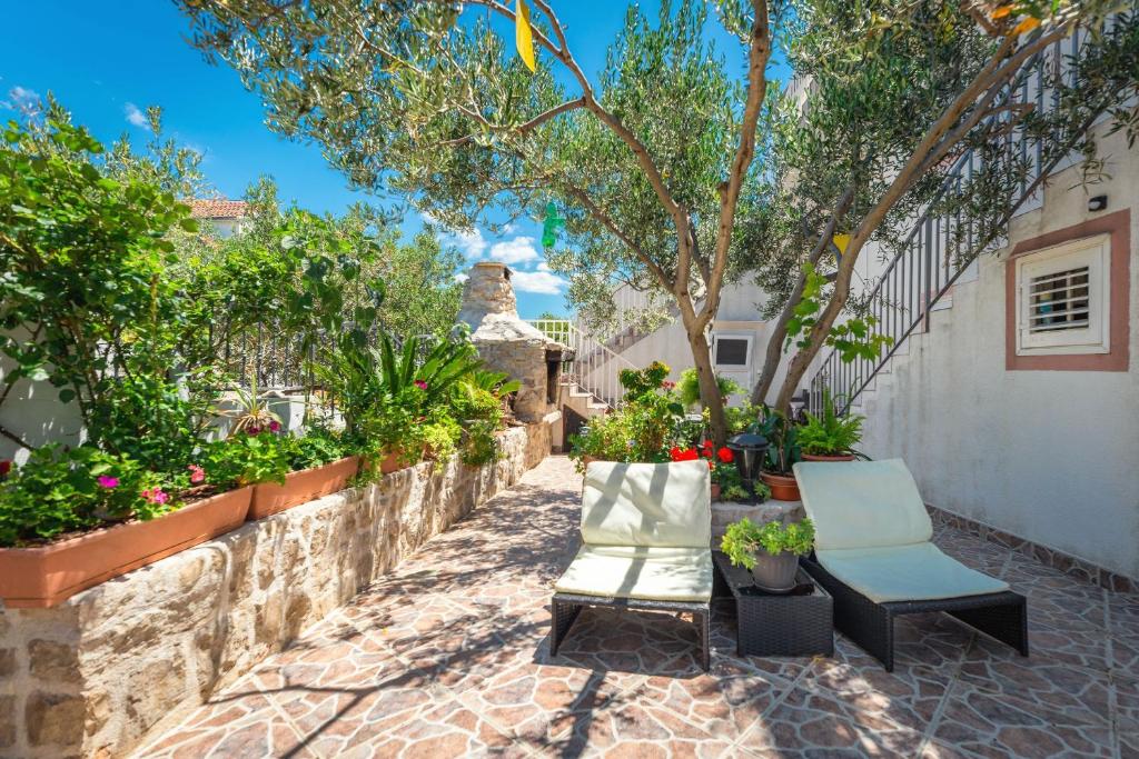 A serene outdoor area is framed by lush greenery and vibrant flowers. Two loungers are positioned on a patterned stone surface, inviting relaxation. A barbecue grill and staircase are visible in the background, enhancing the space's functionality for outdoor enjoyment.