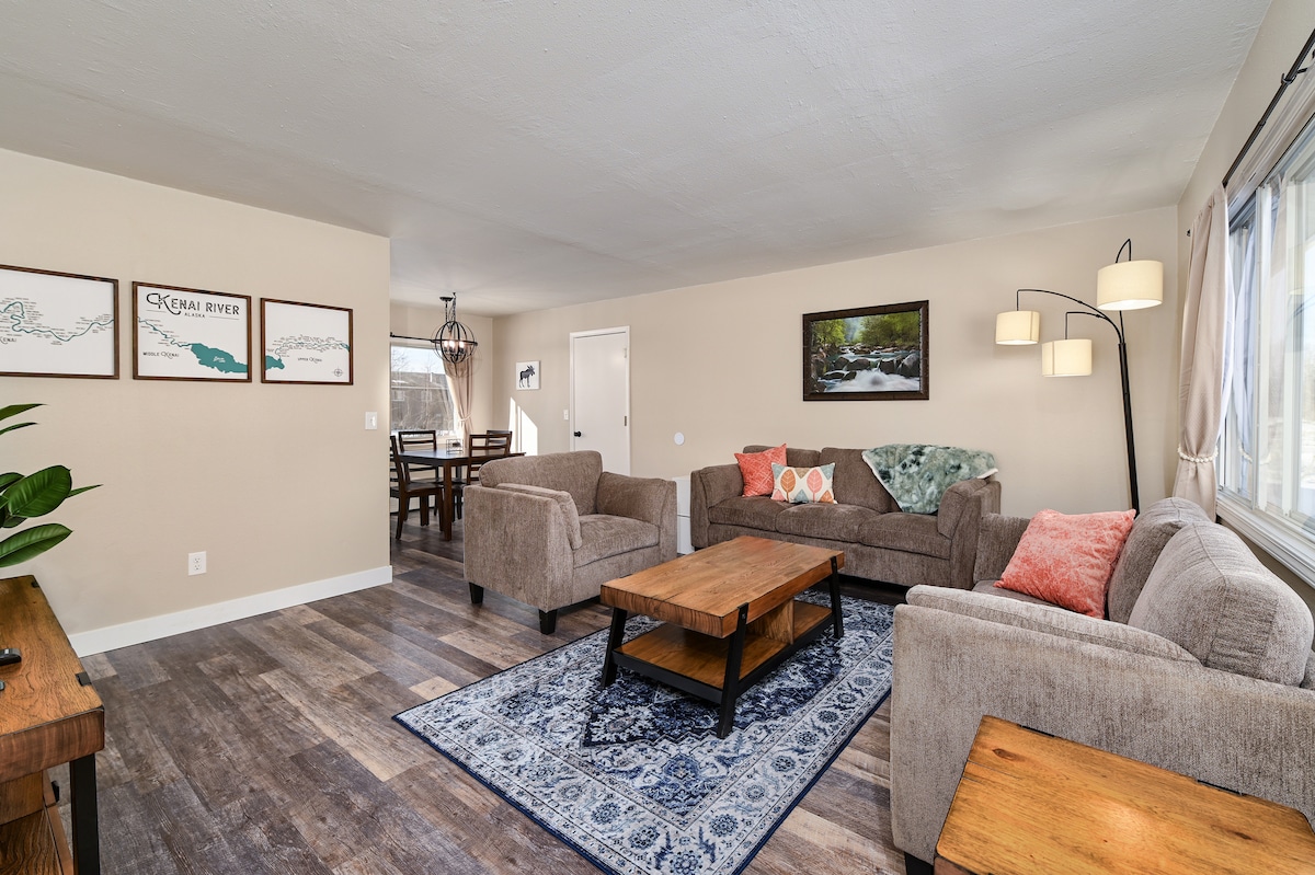 A spacious living area is presented, featuring two comfortable sofas and a wooden coffee table. A decorative area rug adds a touch of warmth to the floor. Natural light enters through the nearby window, illuminating the inviting decor and creating a relaxing atmosphere.