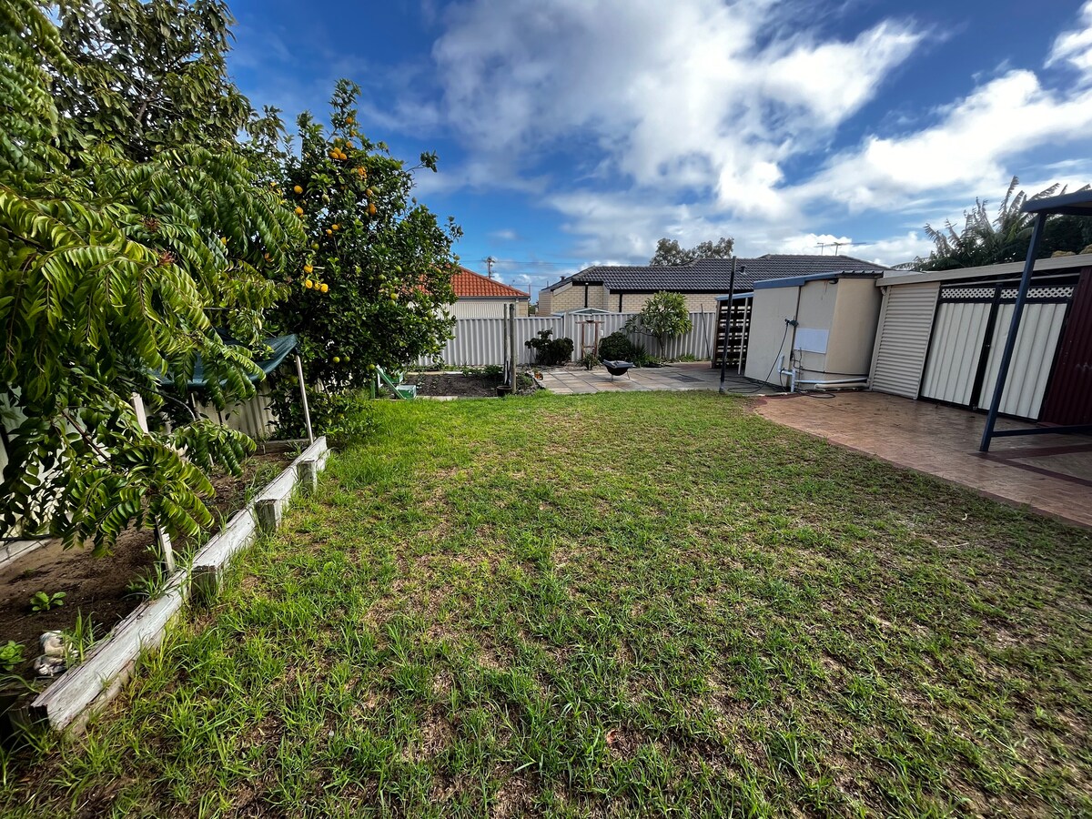 A spacious outdoor area features a well-maintained lawn surrounded by various plants and trees. The courtyard incorporates a mixture of paved and grassy sections, with a garden bed and a gazebo visible in the background.