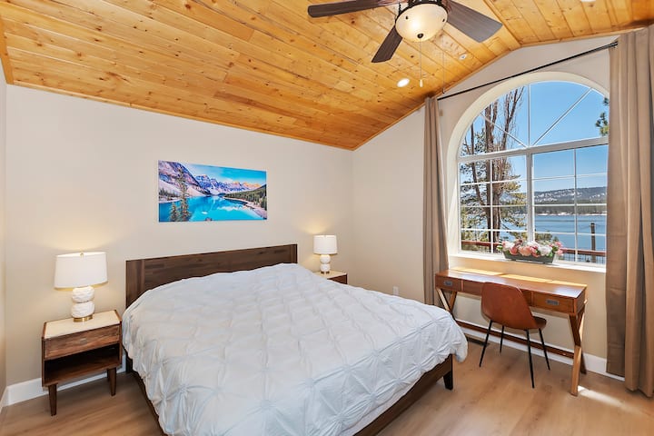 Izba 1 (hlavná) s manželskou posteľou King, pohodlným penovým matracom, stropným ventilátorom a písacím stolom s výhľadom na jazero cez veľké oblúkové okno.