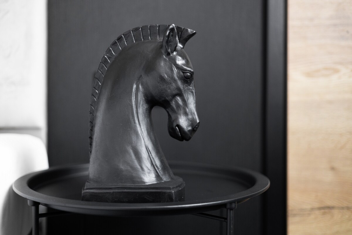 A sleek black horse sculpture rests on a round table. The detailed features of the horse's head are highlighted against a darker background, emphasizing its artistry. Subtle textures of the materials surrounding it contribute to the modern decor of the room.