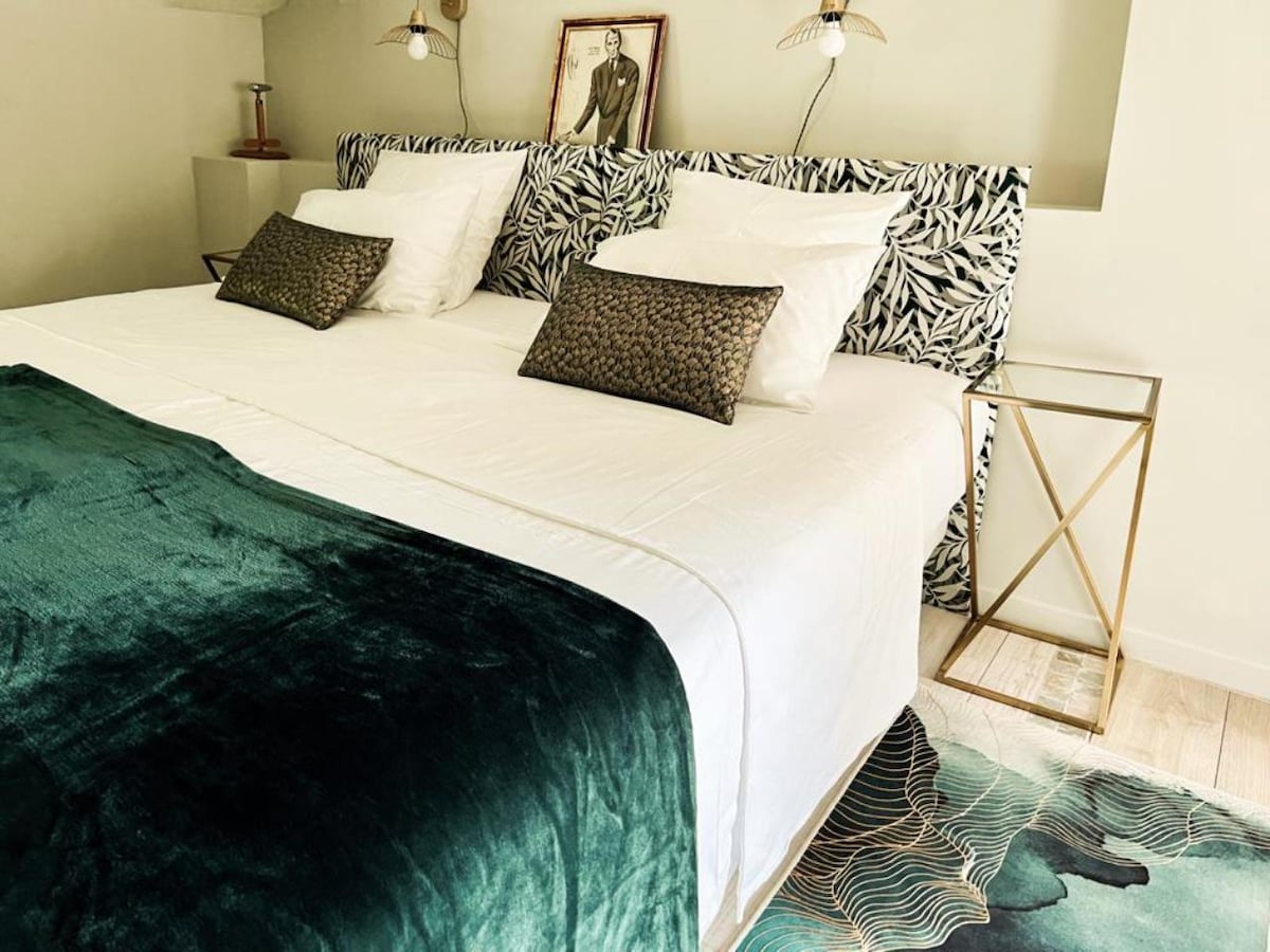 A comfortable sleeping area features a spacious bed with elegant bedding and two decorative throw pillows. A patterned headboard adds a touch of style, while soft lighting is provided by wall sconces on either side. A textured area rug can be seen beneath the bed.