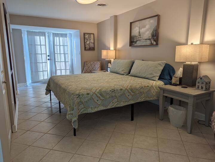 Hlavná spálňa s manželskou posteľou King a dvoma čalúnenými stoličkami. Francúzske dvere vedú na malú oplotenú trávnatú plochu a terasa z červených tehál je hneď za zadným rohom domu.