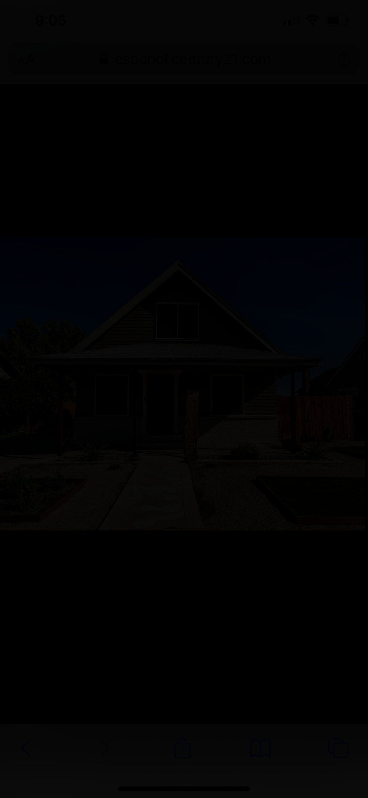 A two-story home showcases a pitched roof and light brown exterior. The front porch features a welcome sign and is bordered by gravel and a small garden, while a wooden fence adds privacy in the background.