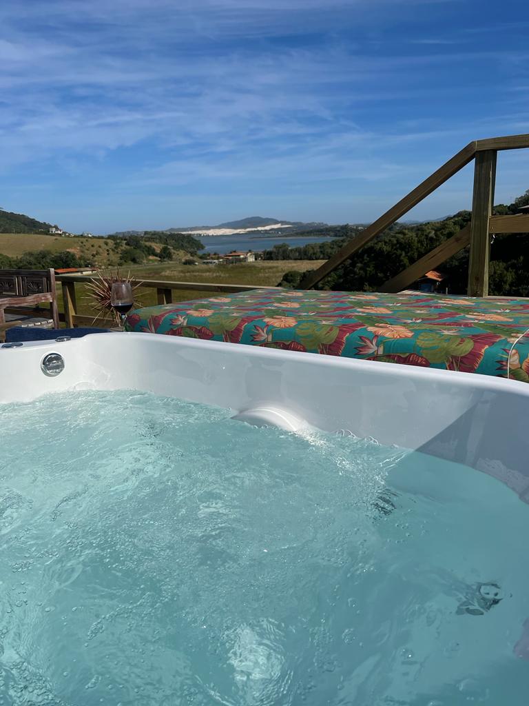 A jacuzzi is filled with clear water, set against a backdrop of rolling hills and a glistening lagoon. Colorful outdoor cushions provide a pop of color on the nearby seating area, enhancing the view of the natural landscape.