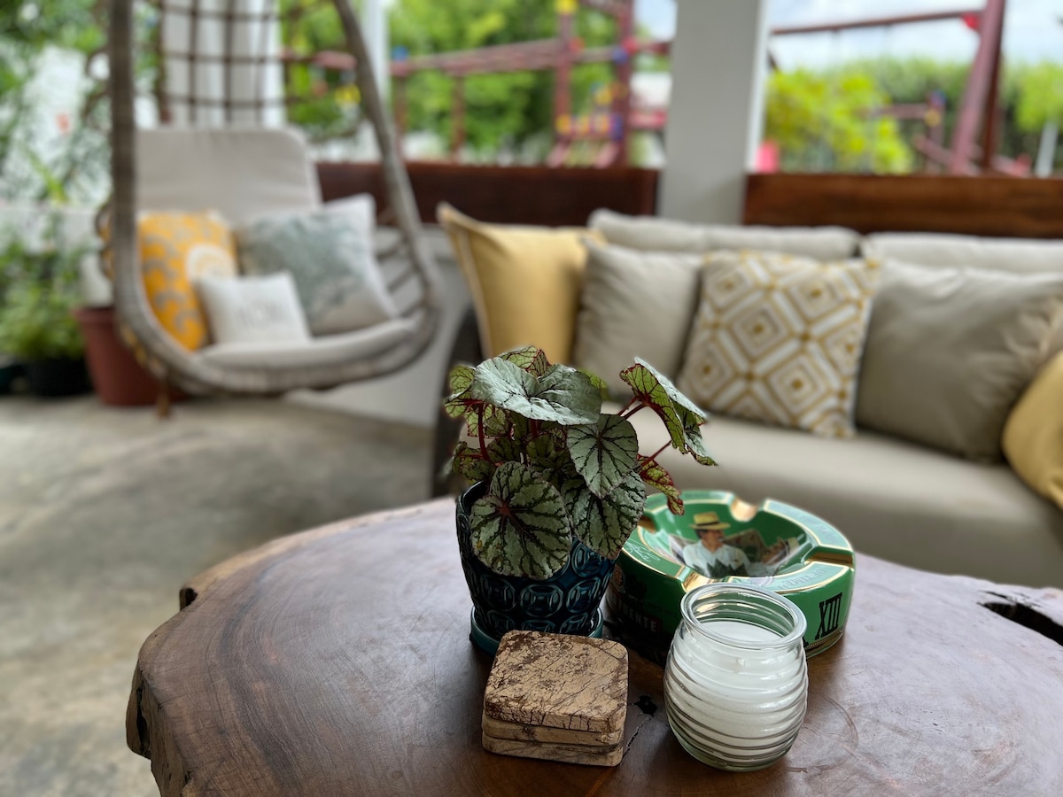 A cozy seating area features a smooth wooden table adorned with a small potted plant, a decorative bowl, and a candle. Soft cushions decorate a nearby couch, enhancing a relaxed and inviting ambiance in the outdoor space.