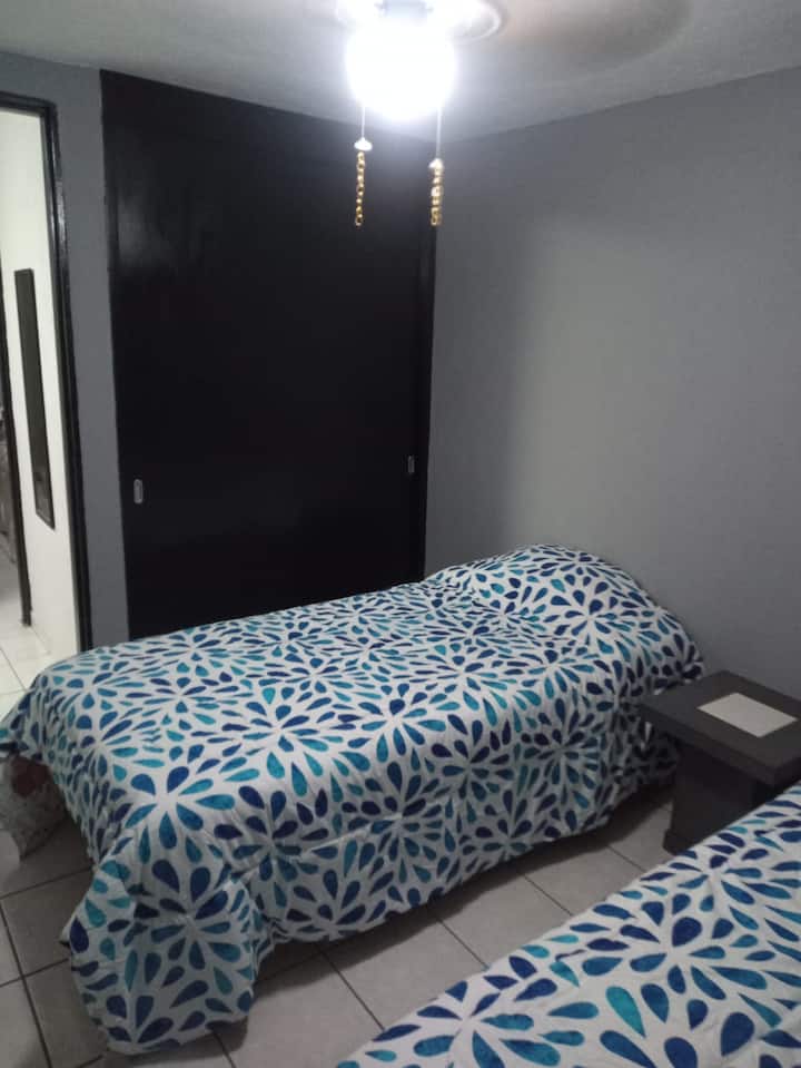 Recámara 2, con dos camas individuales, ventilador, closet y mesa para colocar artículos.