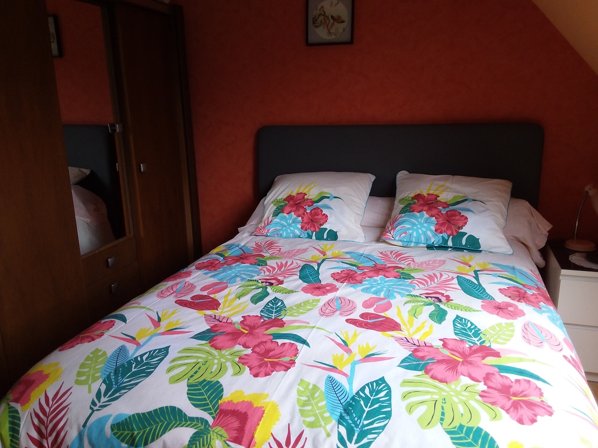 A cozy sleeping area features a spacious bed adorned with a colorful floral duvet cover and matching pillows. Richly textured walls in a warm shade create an inviting backdrop, while a wooden wardrobe is positioned nearby, adding functional elegance to the room.