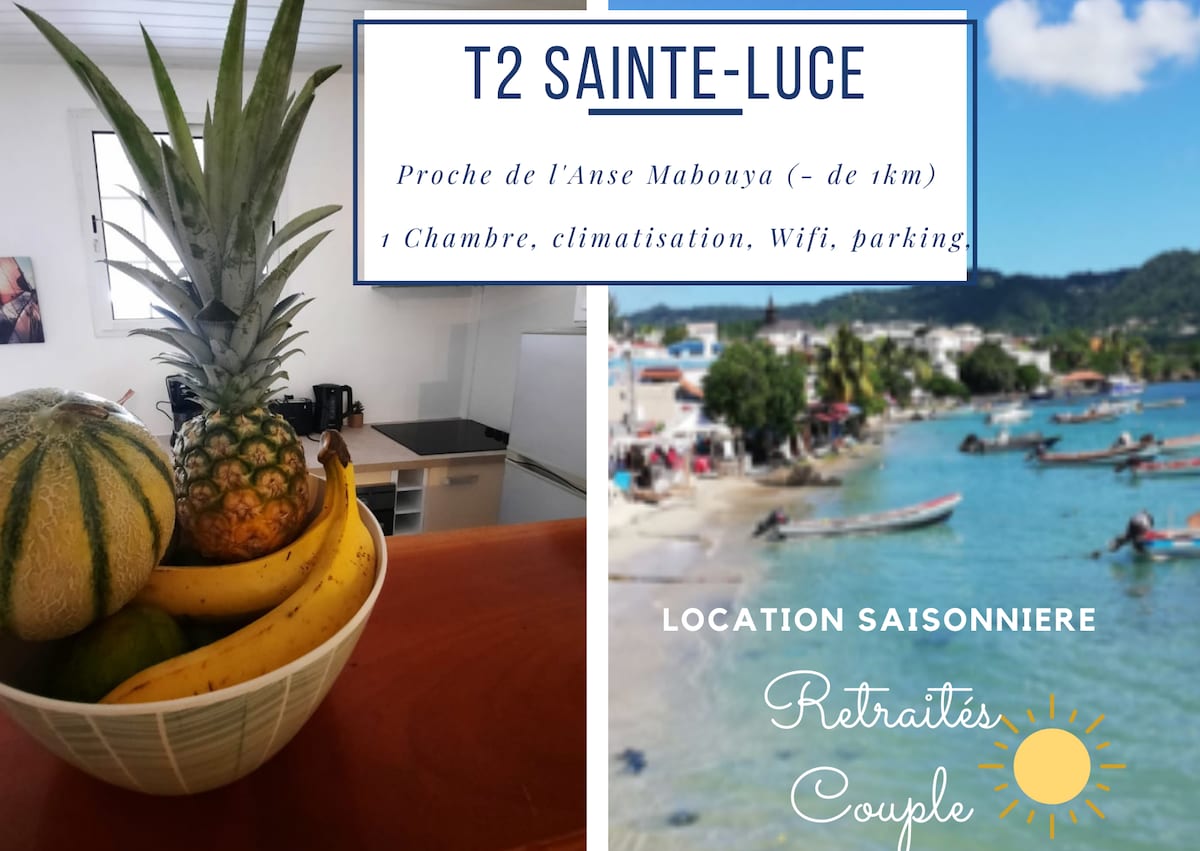 A vibrant bowl filled with an assortment of tropical fruits, including pineapples and melons, sits on a countertop. The background features a view of a calm beach with boats anchored near the shore, highlighting the serene coastal setting.