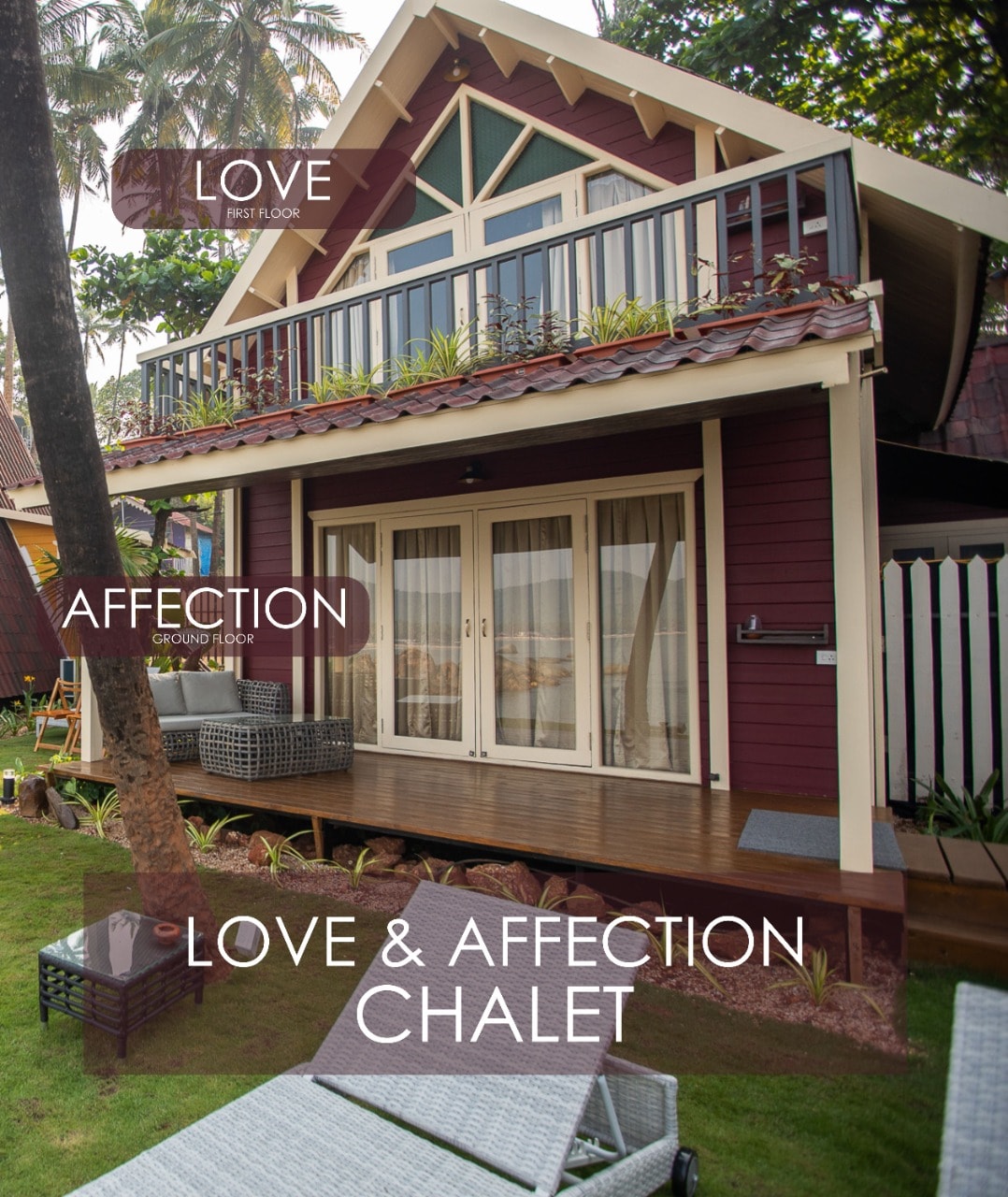The exterior of the Love & Affection chalet is styled with a red facade, featuring a balcony on the first floor. The ground floor is accessible, with an inviting patio area furnished with comfortable seating. Lush greenery surrounds the chalet, enhancing its tranquil atmosphere.