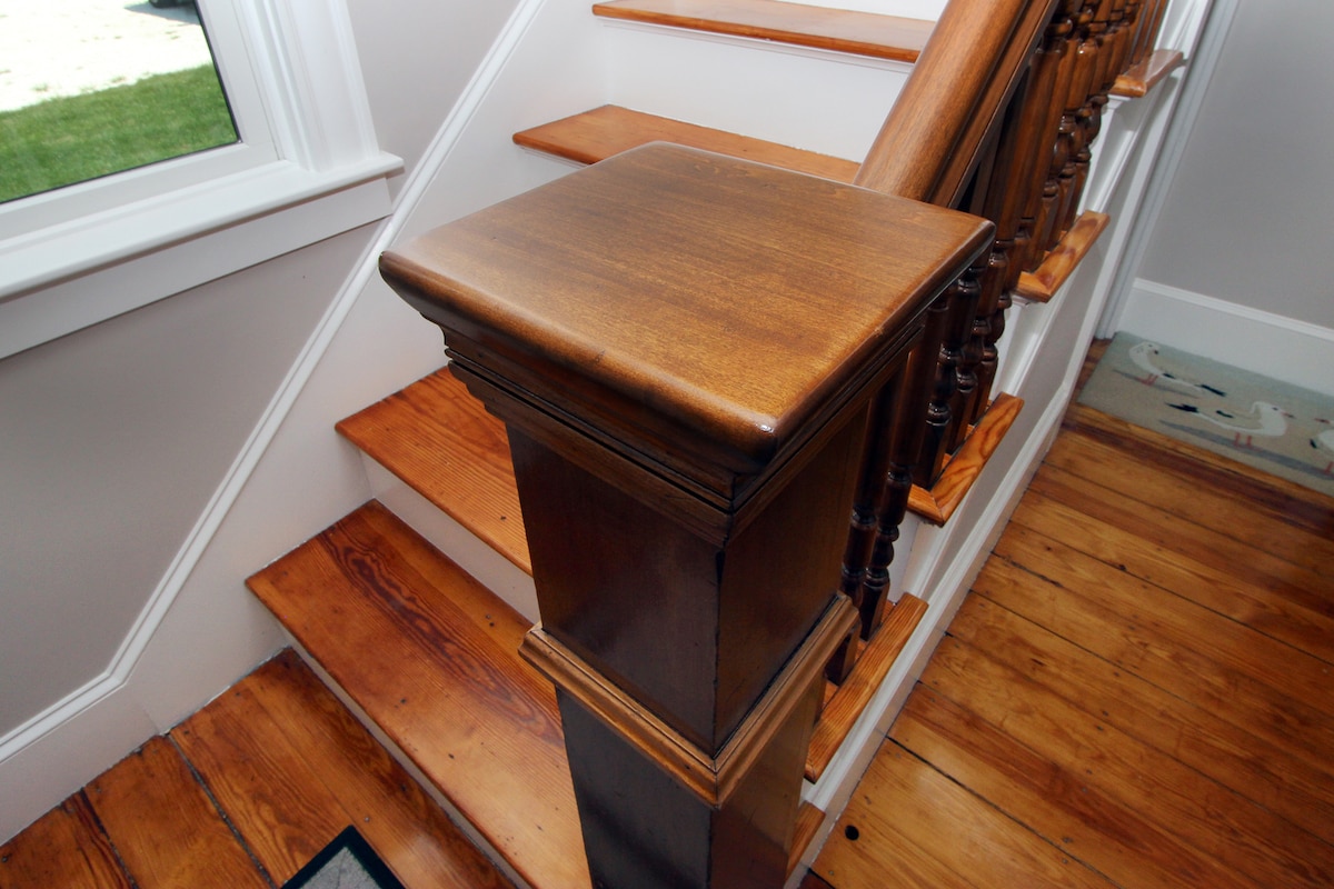 Wooden stairs lead upward, showcasing polished handrails and a smooth newel post. Natural light filters through a nearby window, illuminating the warm hues of the wooden steps and floor. The design elements suggest an inviting transition to the upper levels of the home.