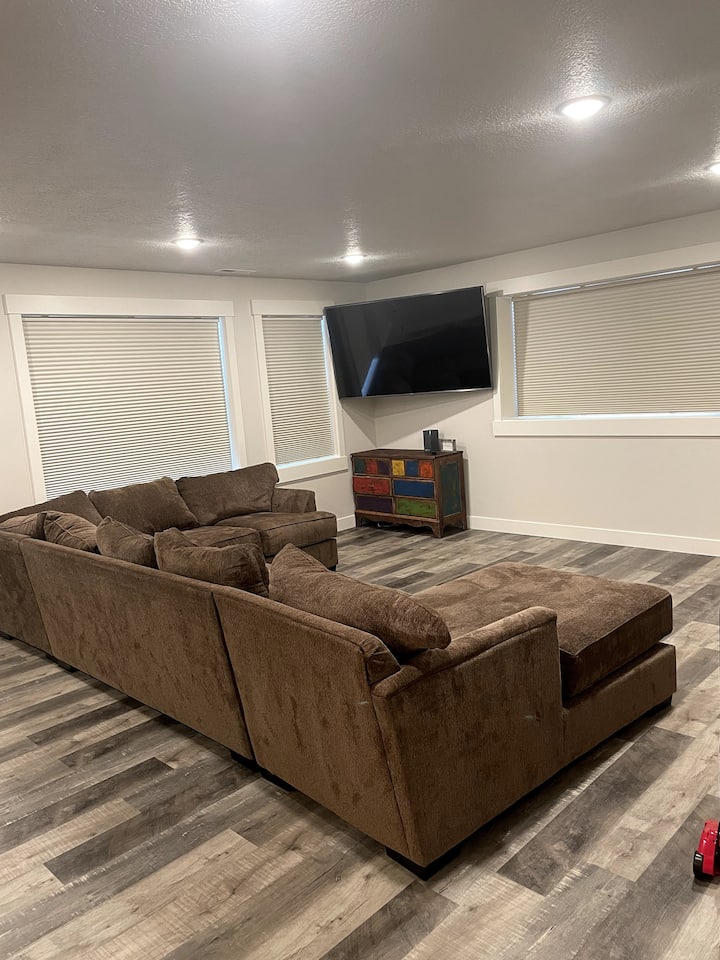 Prostorija za rekreaciju u podrumu s velikim prostorom s kaučem na razvlačenje, TV-om od 75"i zavjesama za zamračivanje za fantastično opuštanje.