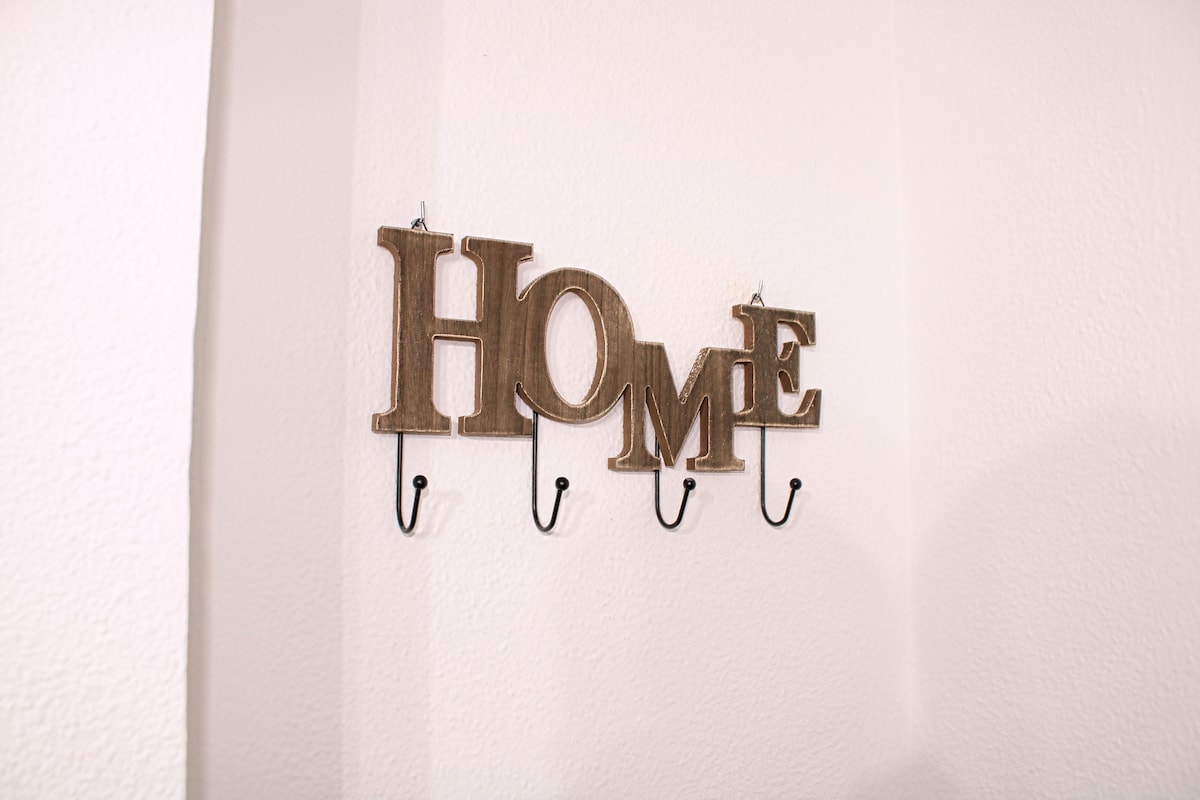 A wall-mounted decor piece displays the word 'HOME' in wooden letters, attached to four hooks for hanging items. The background features a textured light-colored wall.