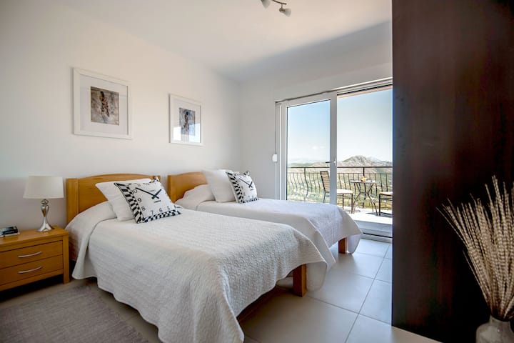 DVOKREVETNA SPAVAĆA SOBA IZ KOJE SE IZLAZI NA BALKON S POGLEDOM NA MORE, GARDEROBEROM I SUSJEDNOM KUPAONICOM S KLIMA-UREĐAJEM.