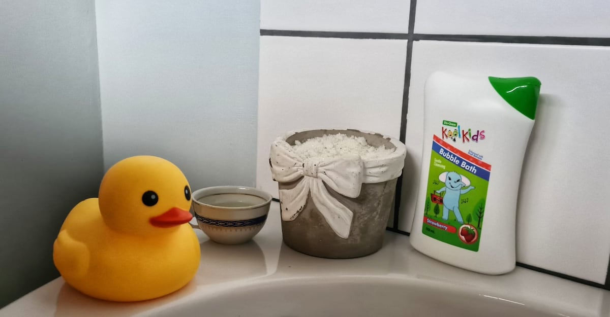 A playful bathroom scene is captured, featuring a cheerful yellow rubber duck alongside a small bowl and a decorated container filled with bath salts. A bottle of children's bubble bath is prominently displayed, adding a touch of whimsy to the relaxing atmosphere.