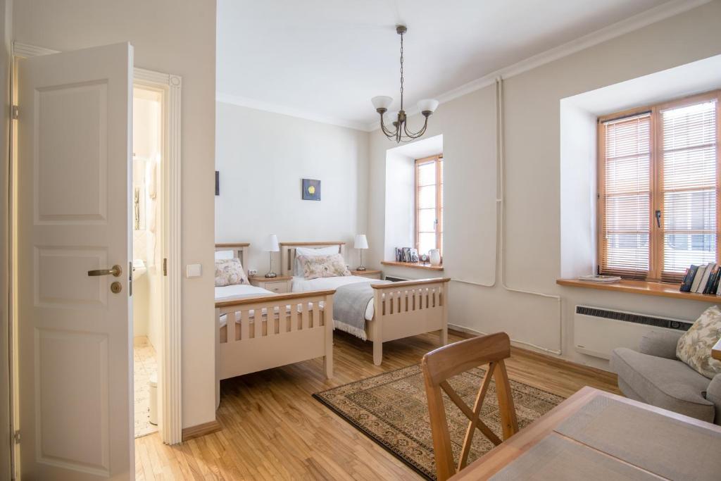 A well-lit studio apartment is showcased, featuring two spacious beds with light-colored wooden frames. Natural light enters through two large windows, illuminating the oak flooring. A cozy seating area and a dining table are visible, contributing to a functional living space.