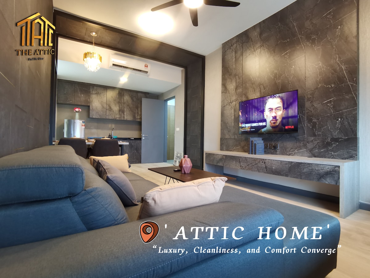 A modern living space features a spacious gray sofa complemented by a stylish coffee table. A sleek entertainment unit holds a large flat-screen TV, while the kitchen is visible in the background, showcasing contemporary cabinetry. Soft lighting enhances the clean and inviting environment.