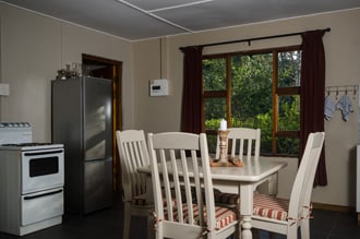 A dining area is presented with a rectangular table surrounded by six light-colored chairs. A bright window allows natural light to fill the space. A stainless steel refrigerator stands beside a white stove, enhancing the kitchen essentials.