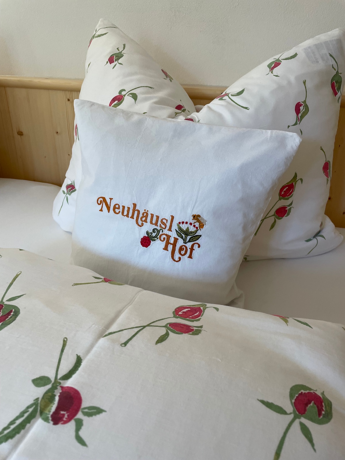 A cozy bedding arrangement showcases pillows featuring a floral design with embroidered text. The soft fabric and delicate rose patterns complement the light-coloured sheets, creating a calming atmosphere in the room.