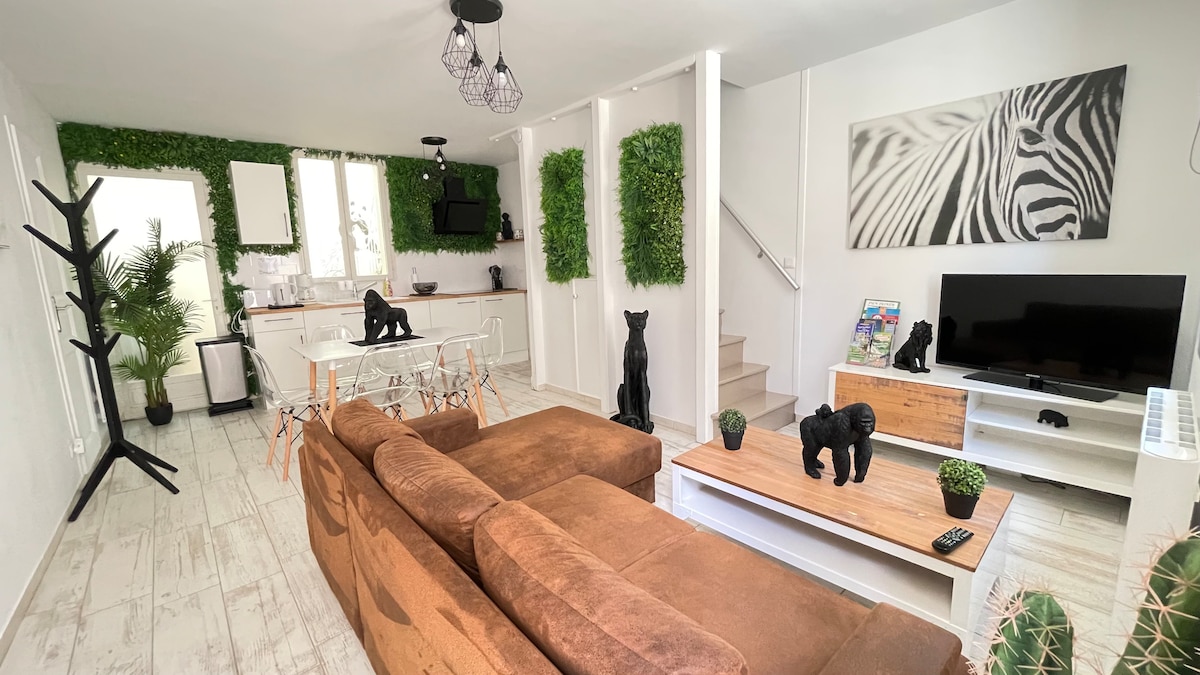 An open living space showcases a brown sectional sofa complemented by a wooden coffee table. A dining area features a glass table surrounded by transparent chairs. Green wall accents and decorative figurines add character, while a TV is positioned on a white media console.