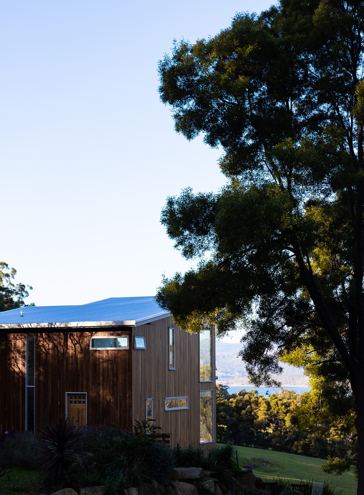 The exterior of Wildwood Retreat is highlighted, showcasing a modern wooden structure with large windows that offer glimpses of the surrounding landscape. Lush trees frame the view, creating a sense of seclusion. The sky above is clear, enhancing the tranquil atmosphere.