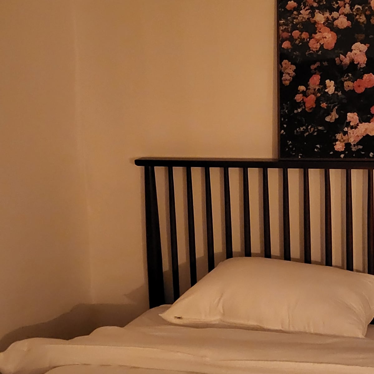 A cozy sleeping area features a wood bed frame with a floral headboard. Soft bedding is arranged on the bed, complemented by a plush pillow. The warm, neutral tones of the walls create a serene backdrop.