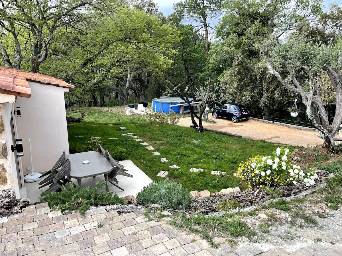 A serene outdoor area is showcased, featuring a grassy space with garden pathways and a seating arrangement of a round table surrounded by chairs. A blue above-ground pool is visible, alongside a parked car and mature trees enhancing the natural setting.