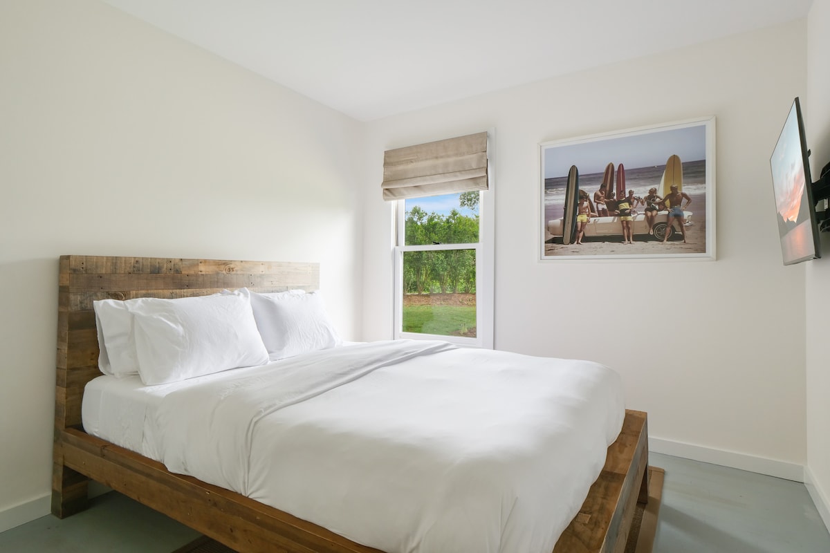 Dhoma e gjumit 3 me televizor të montuar në mur, dollap dhe pamje nga kopshti i përparmë.