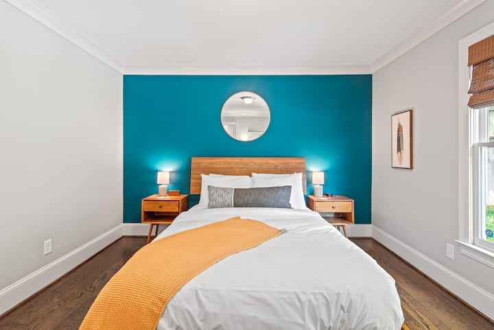 Striking teal accent wall with round mirror, queen bed & dual lamps. Mid-century design in this East Atlanta Airbnb Guest Favorite. Pack n play and baby essentials on site.