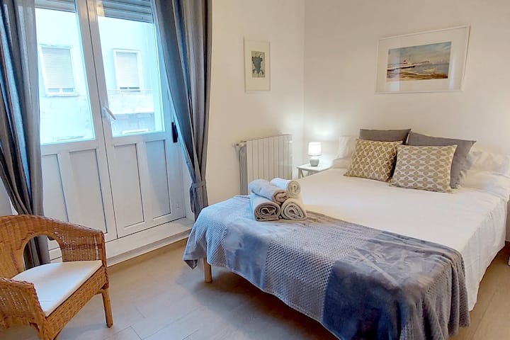 Втора спална соба со мал двоен кревет, плетен стол и огледален плакар.